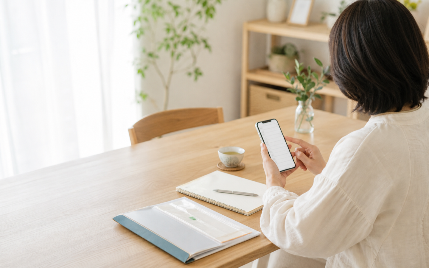 明るいダイニングでスマートフォンを使って契約を整理する女性